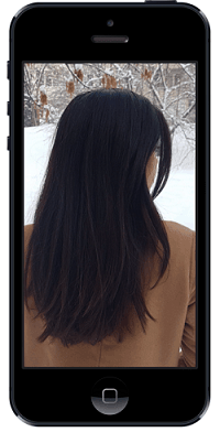 Donna con lunghi capelli neri, vista di spalle, indossa un cappotto marrone in un paesaggio innevato, visualizzata su uno schermo di smartphone.