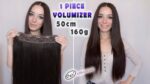 Donna che mostra un volumizzatore per capelli da 50 cm e 160 g, con capelli lunghi e lisci, ideale per aggiungere volume e lunghezza ai capelli naturali.